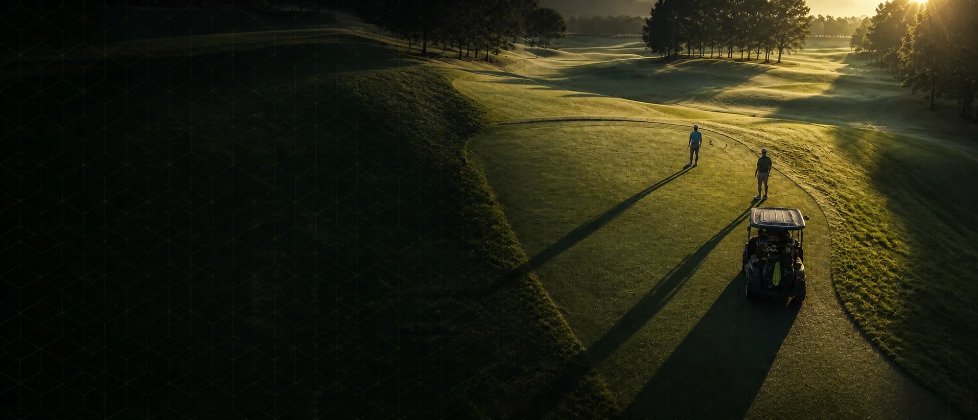 Two golfers walking ahead of their cart across a dew-covered golf course at sunrise